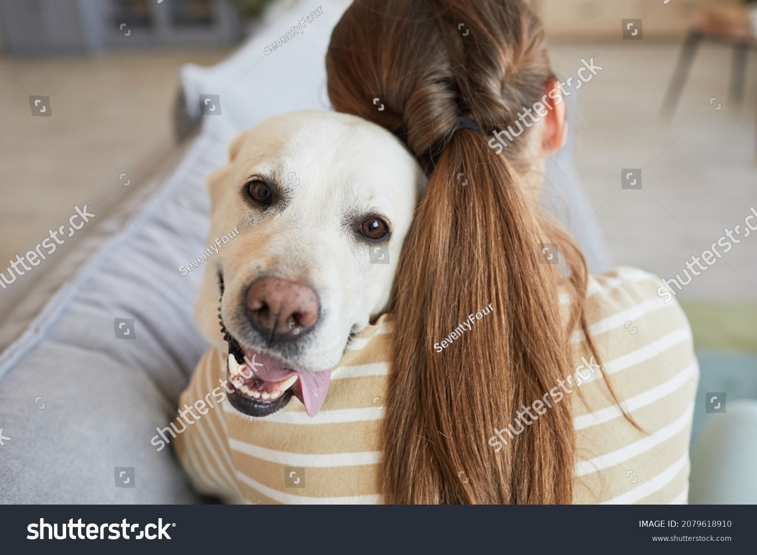 Back view close up of young woman cuddling with dog while lying on couch at home, copy space #2079618910