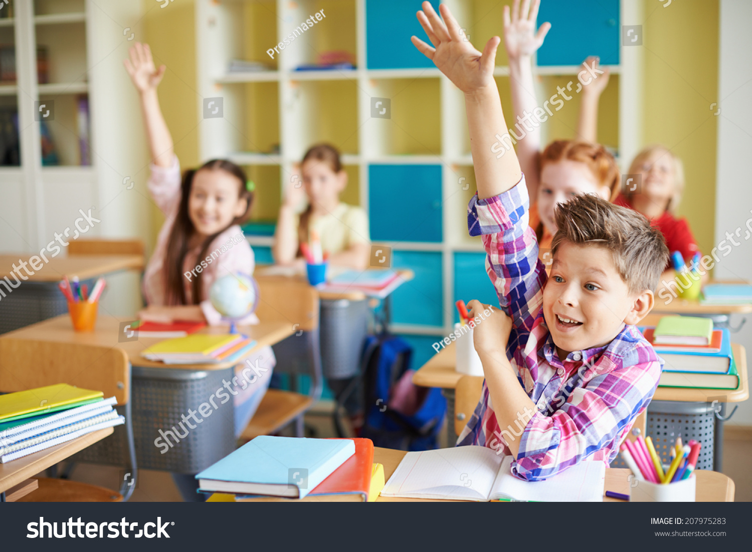 Portrait of cute boy raising hand at workplace with his classmates behind #207975283
