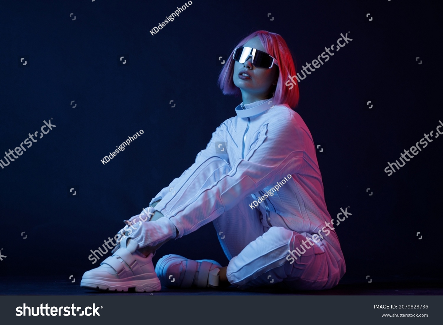 Woman in futuristic costume. Female in modern VR glasses interacting with network while having virtual reality experience. Augmented reality game, future technology, AI concept. VR. Neon blue light. #2079828736