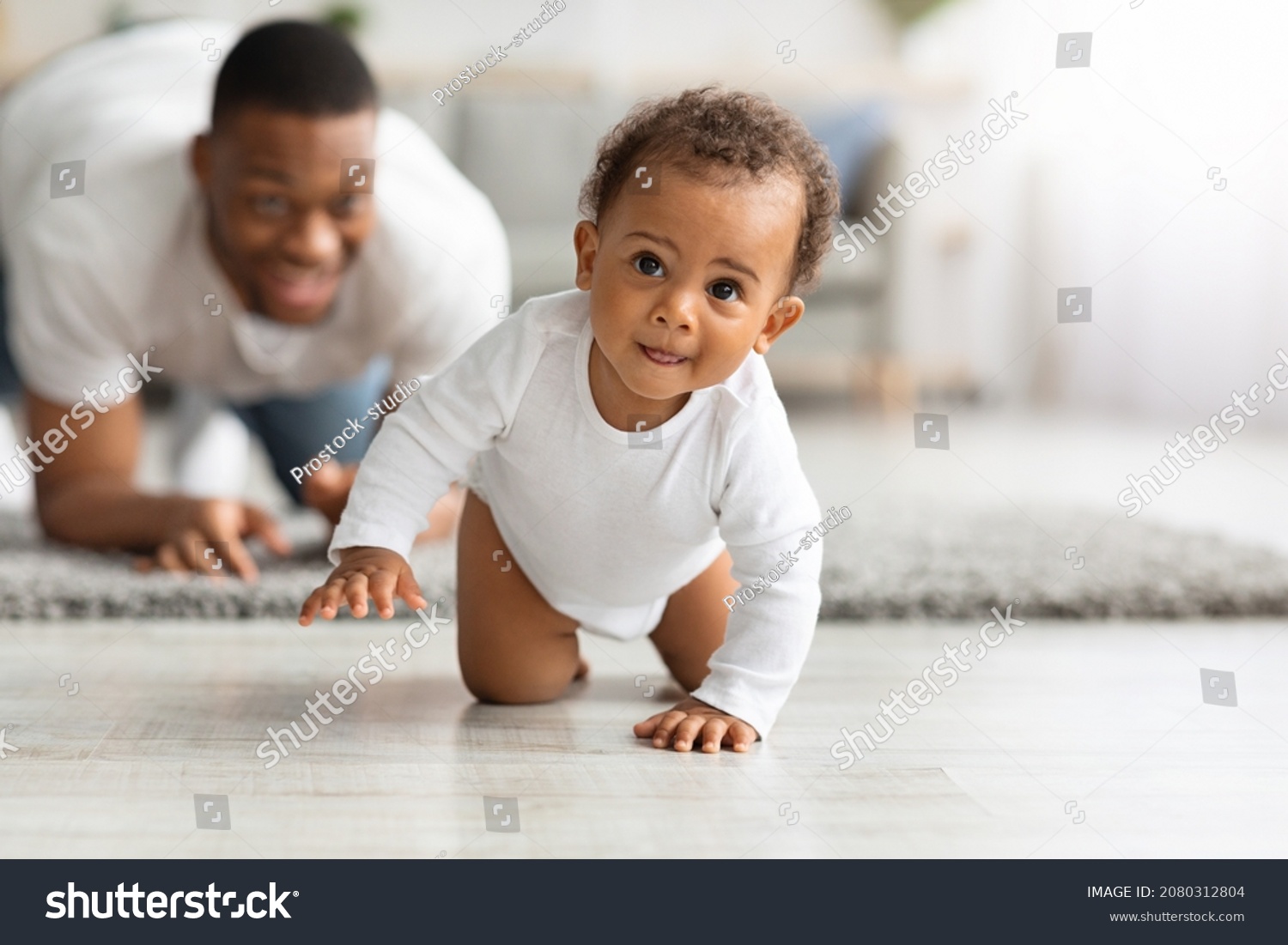 Cute Little Black Infant Baby Crawling On Floor At Home, Proud Young Father Looking At Him And Smiling, Dad And Toddler Child Enjoying Spending Time Together, Selective Focus With Copy Space #2080312804