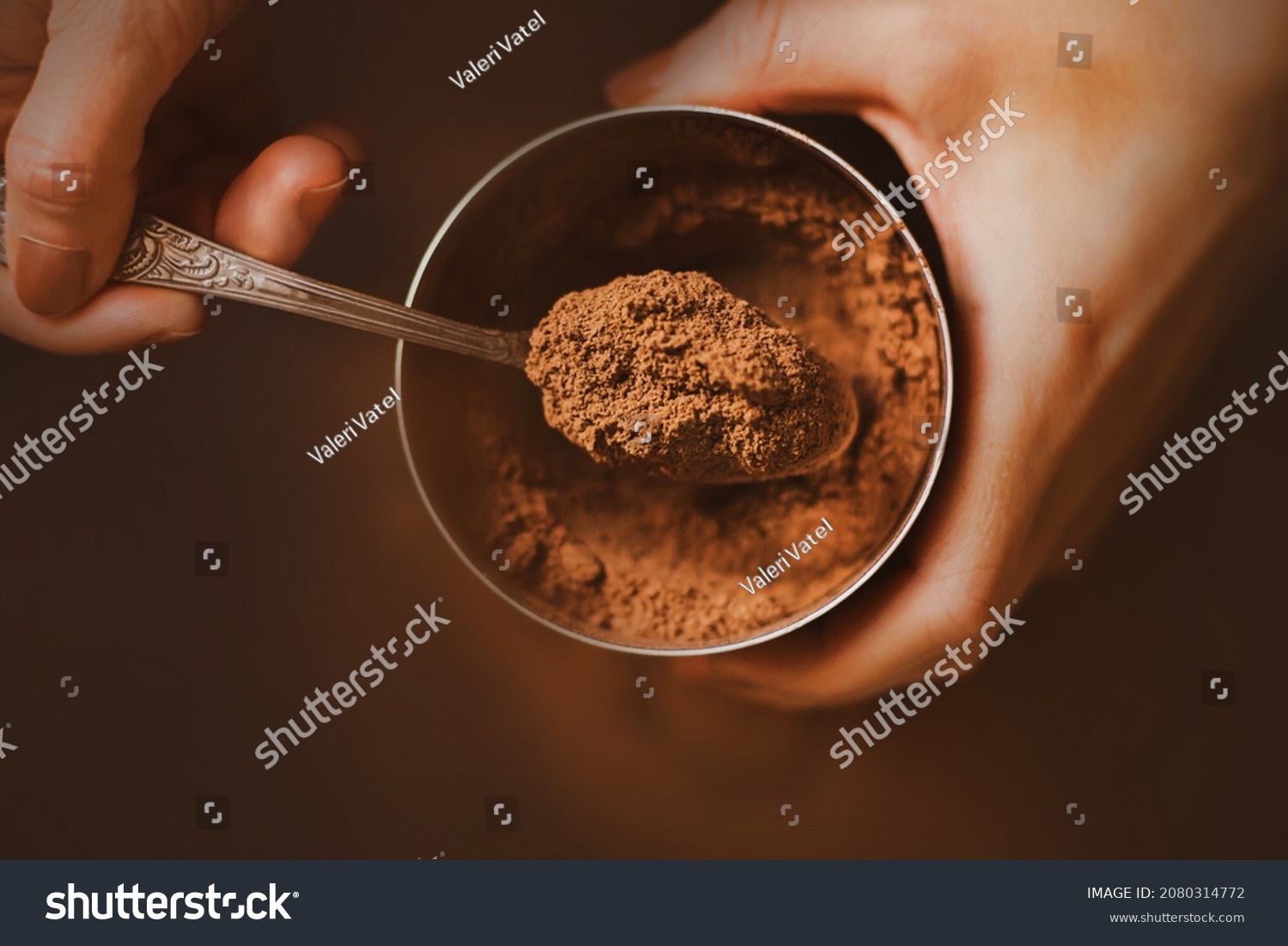 A woman with a brown manicure on her nails holds a jar of fragrant crumbly cocoa powder in her hands and scoops a portion with a silver teaspoon. A delicious drink in the morning. The cooking process. #2080314772