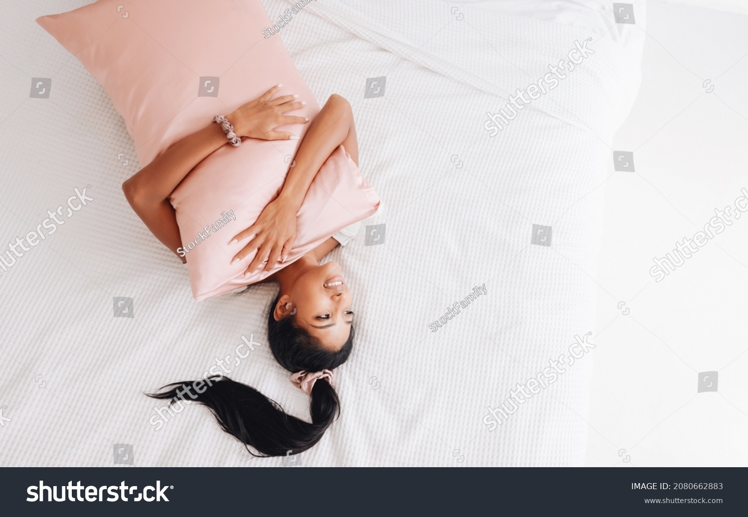 Beautiful Indonesian girl lying on a pink pillow with a silk pillowcase. View from above
 #2080662883