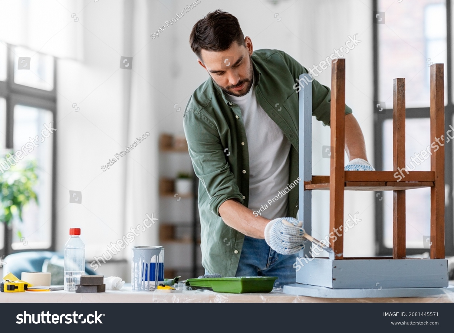 furniture renovation, diy and home improvement concept - man in gloves with paint brush painting old wooden table in grey color #2081445571