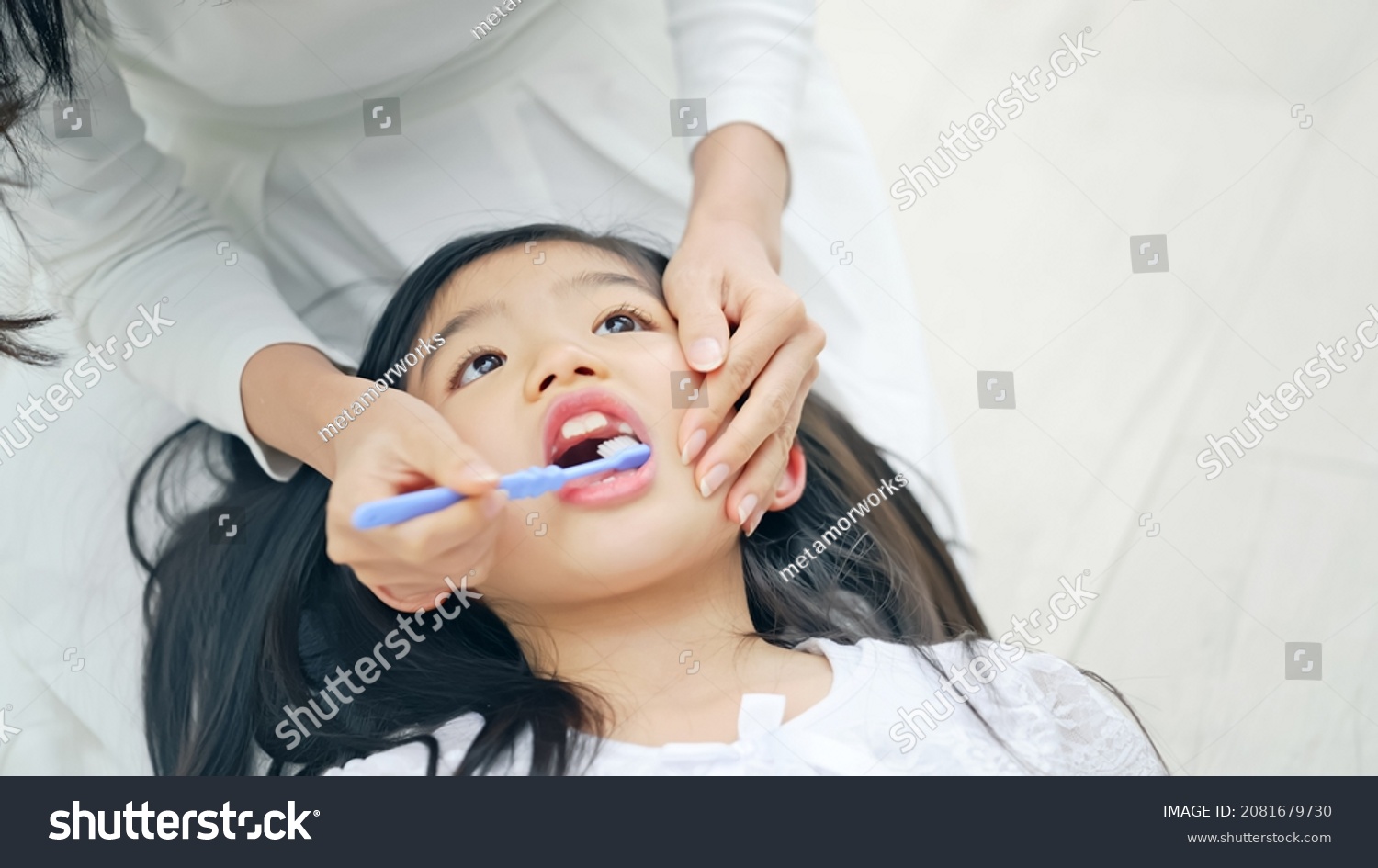 Asian girl having mom brush her teeth. Dental care. Oral care. #2081679730