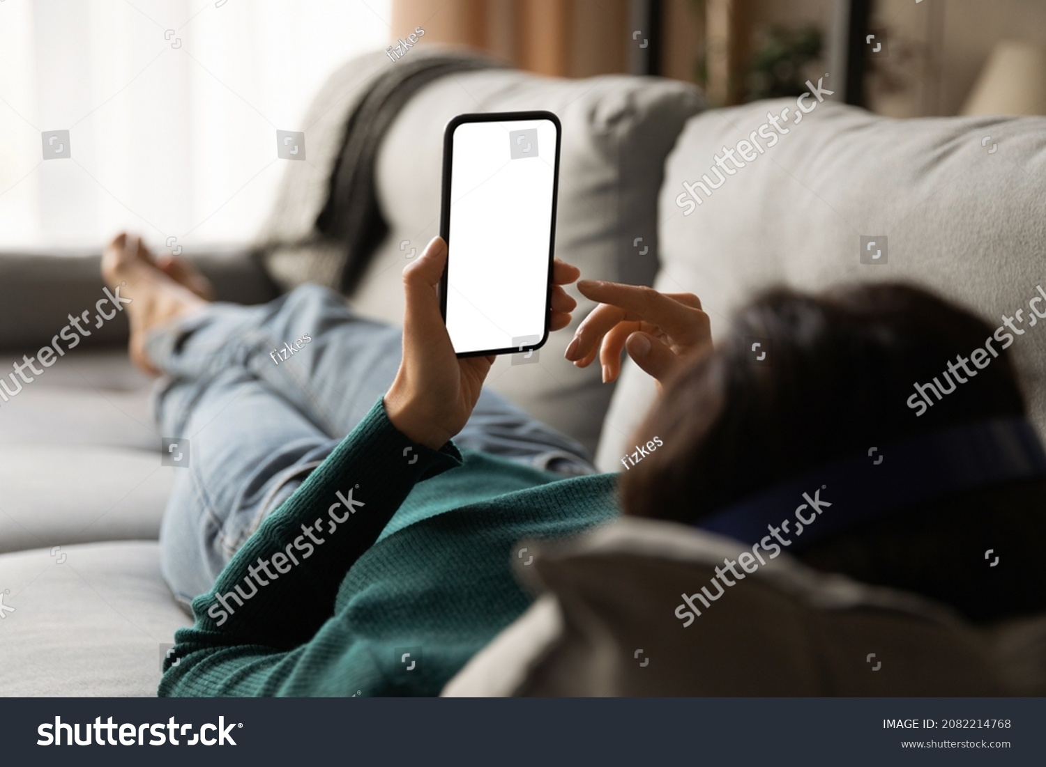 Female using phone. Over shoulder view of young woman lying on sofa hold smartphone with blank empty screen. Template for web app chat interface online advertisement mobile game social network profile #2082214768