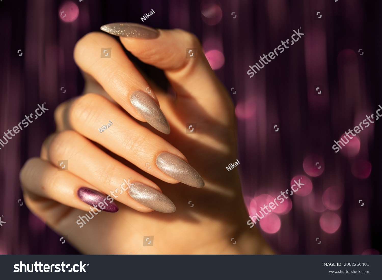 Girl's hand with a beautiful long nails in silver and violet colour on a blurred violet twinkle background #2082260401