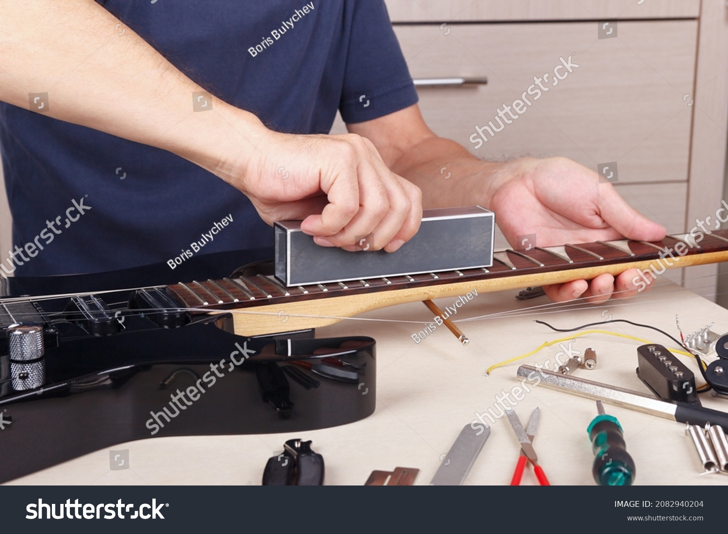 Guitar master aligns the frets on guitar neck with leveling bar. #2082940204