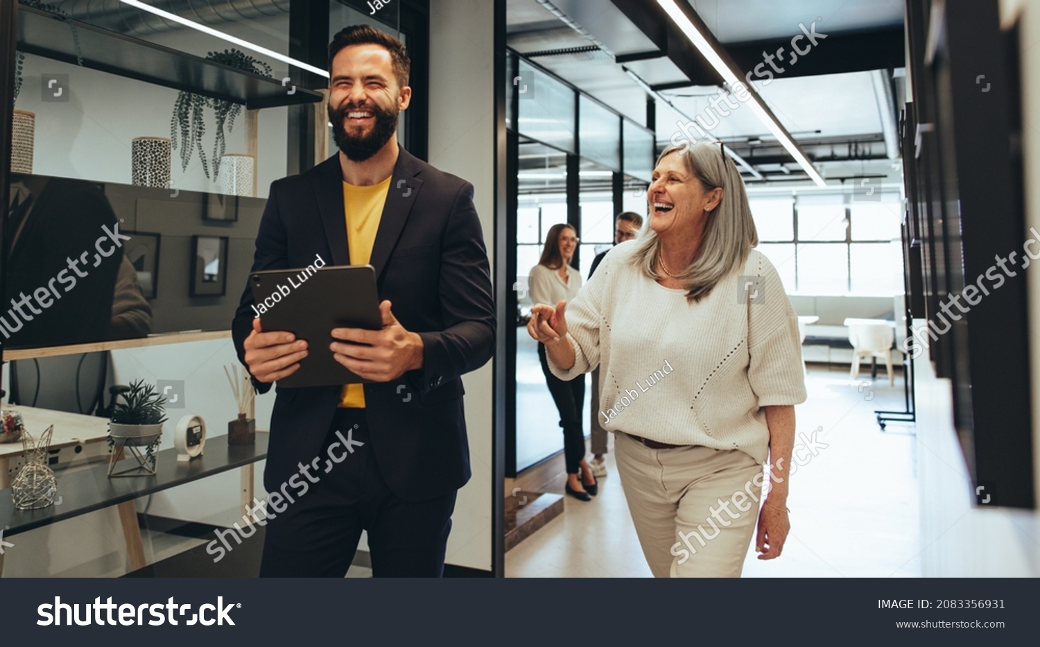 Laughing entrepreneurs walking together in an office. Two happy business colleagues sharing a laugh while having a discussion. Diverse businesspeople working together on a project. #2083356931