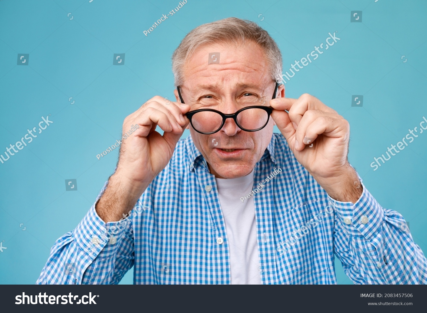 Poor Eyesight. Senior Man Can't See, Squinting Eyes Wearing Glasses Having Problems With Vision, Looking At Camera At Blue Studio. Ophtalmic Issue, Bad Sight In Older Age, Macular Degeneration Concept #2083457506