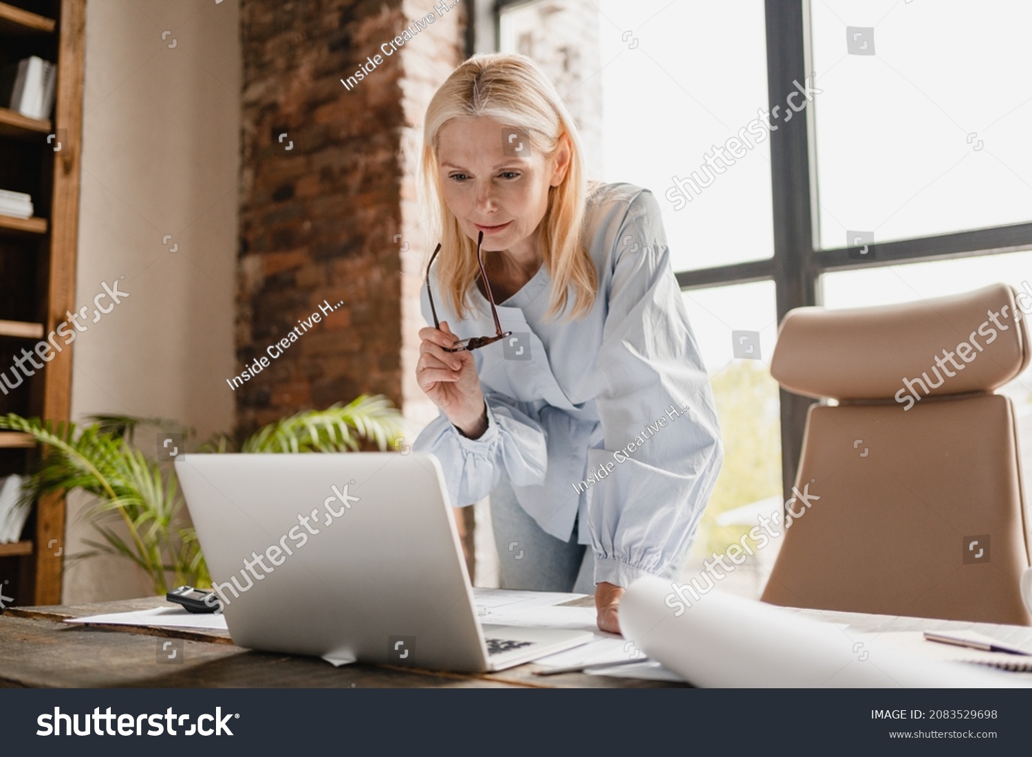 Concentrated caucasian middle-aged mature businesswoman ceo boss typing on laptop, working at office desk with documents, searching surfing web online #2083529698