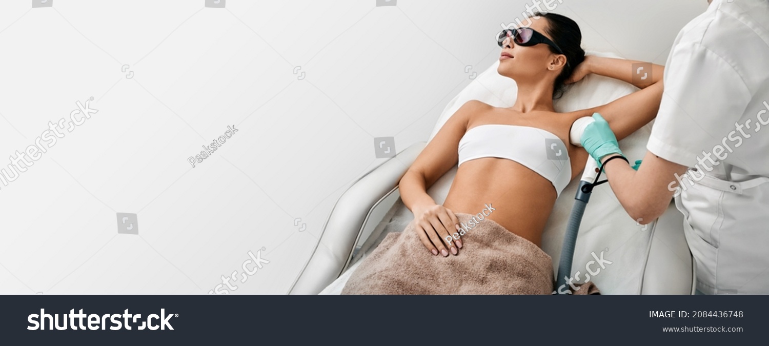 Woman during underarm laser hair removal and armpit laser epilation at beauty center. Laser epilation concept, web banner with space for text #2084436748