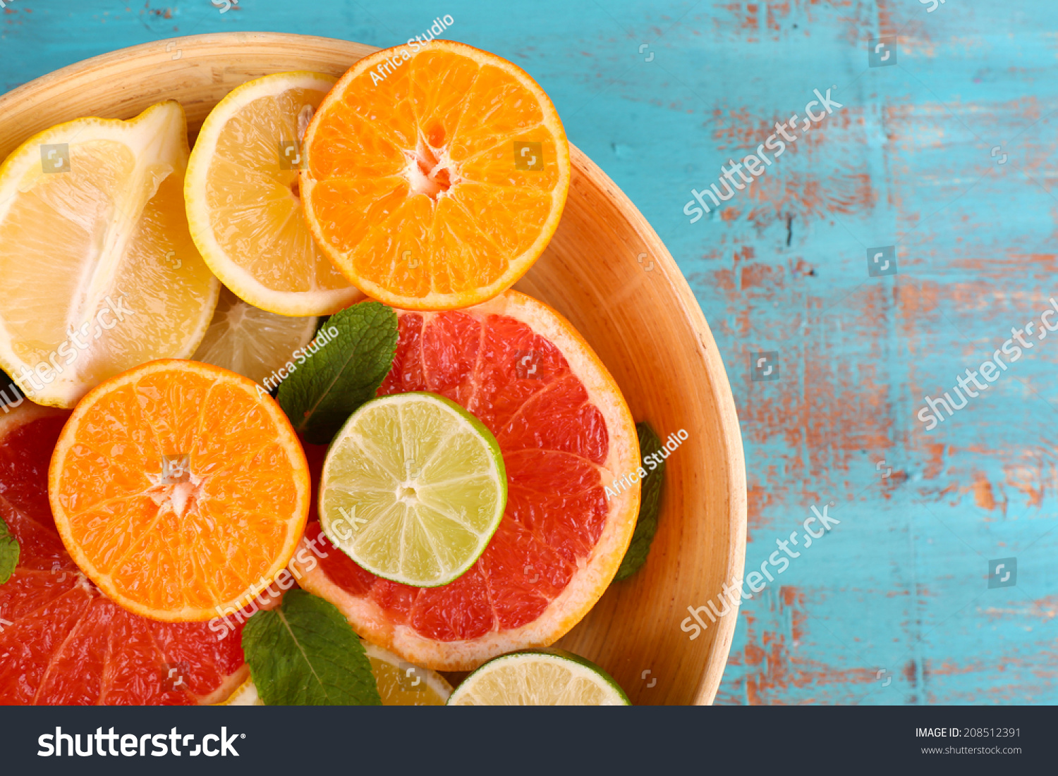Different sliced juicy citrus fruits in bowl on blue wooden table #208512391