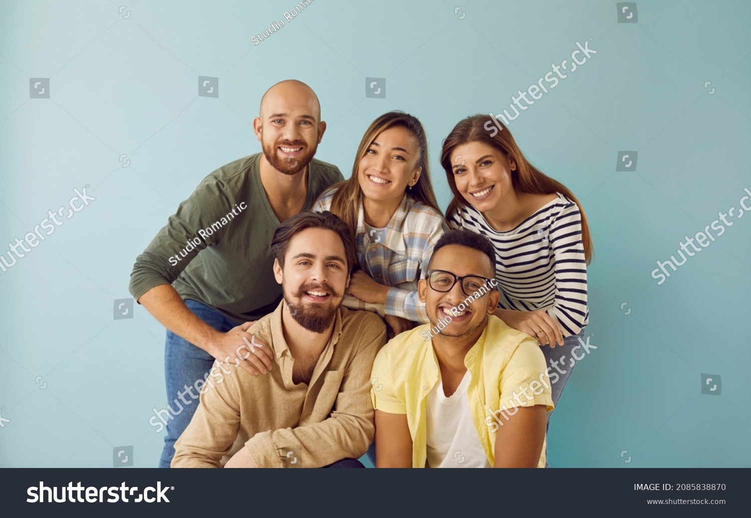Group portrait of five happy, smiling mixed race multi ethnic friends. Team of 5 cheerful young diverse people with toothy smiles having photoshoot and looking at camera against blue studio background #2085838870