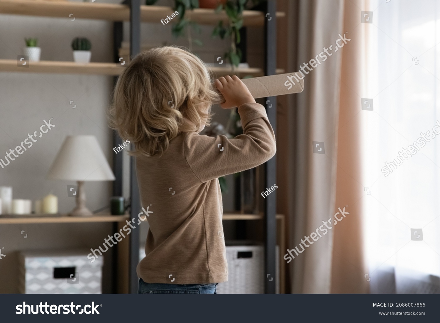 Little preschool adorable boy holding toy cardboard spyglass, looking forward at window at home. Sweet kid playing game with paper homemade craft tube telescope, having fun, imagining adventures #2086007866