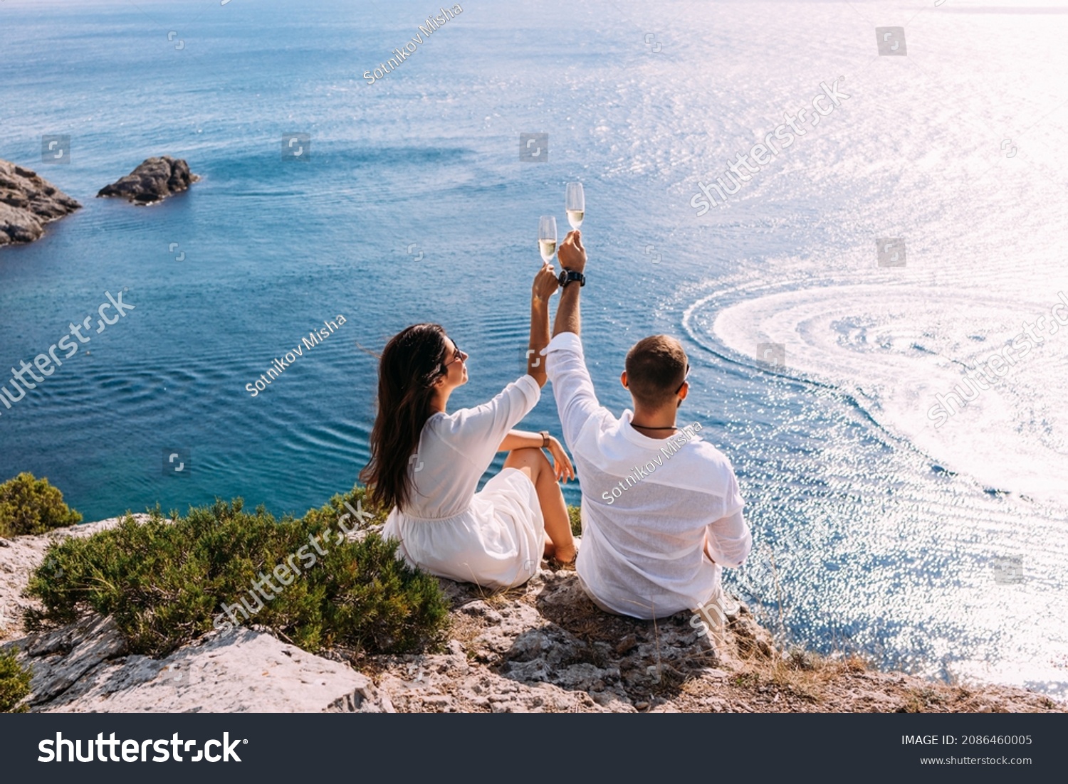 A couple in love celebrates their engagement on the seashore. A beautiful couple drinks champagne by the sea. Honeymoon trip. Lovers on the beach. Wedding travel. Couple on vacation. Copy space #2086460005
