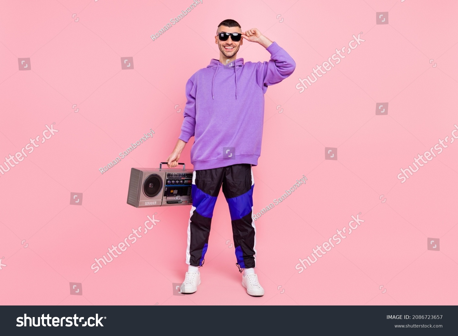 Full size photo of cool young brunet guy with boom box wear eyewear hoodie pants sneakers isolated on pink background #2086723657