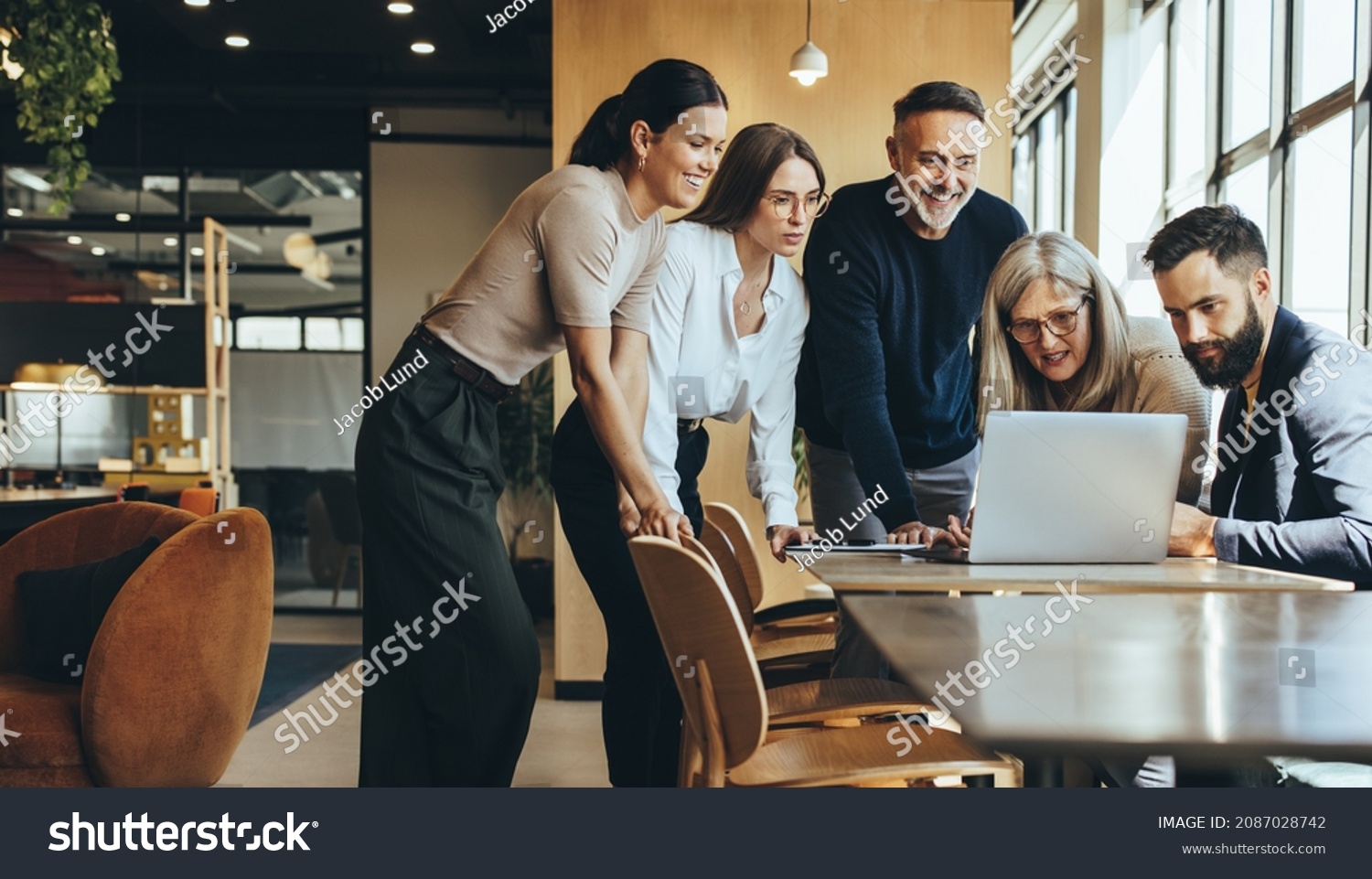 Group of diverse businesspeople using a laptop while collaborating on a new project. Team of happy businesspeople looking at the laptop screen while working together in a modern workspace. #2087028742