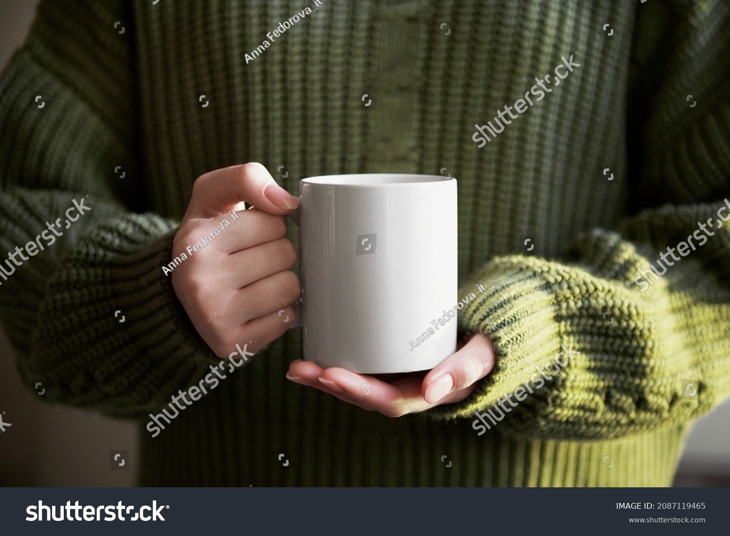 female hand holding white mug with blank copy space for your advertising text message or promotional content, sweet coffee or tea. Girl in green sweater holding white porcelain mug mock up #2087119465
