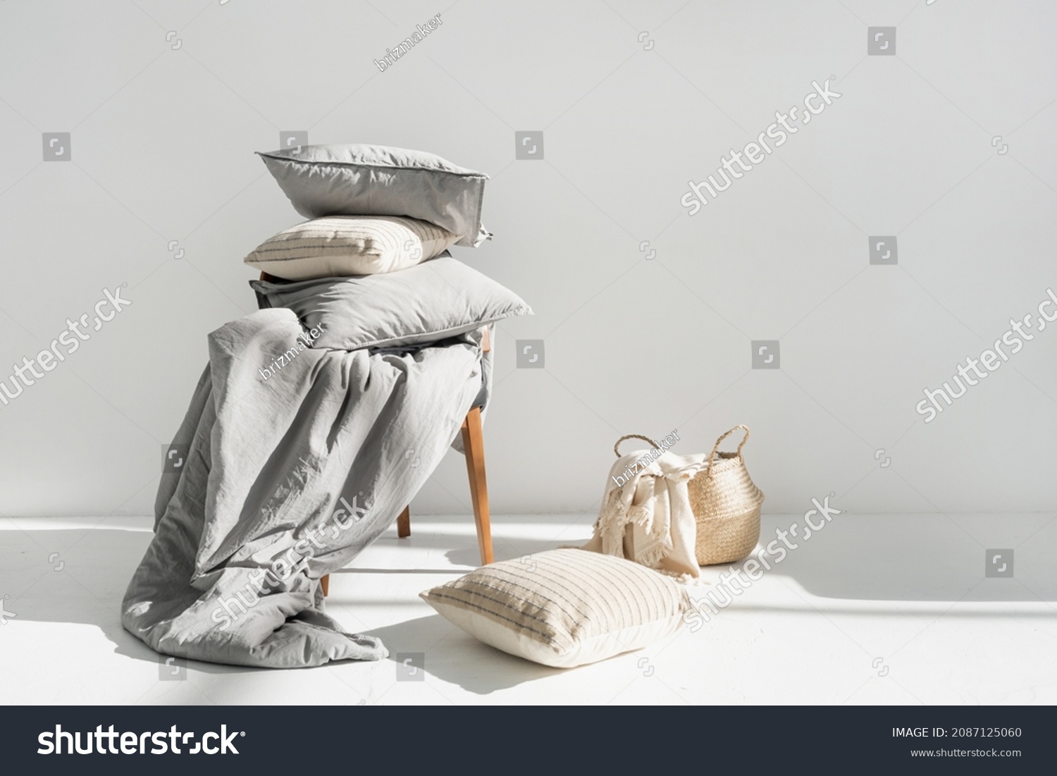 Plaid in wicker basket, clean blanket, linen bedding, cotton sheets, pillow, cushion and duvet with natural material on chair after laundry, copy space. Washing, housekeeping, hotel service concept #2087125060