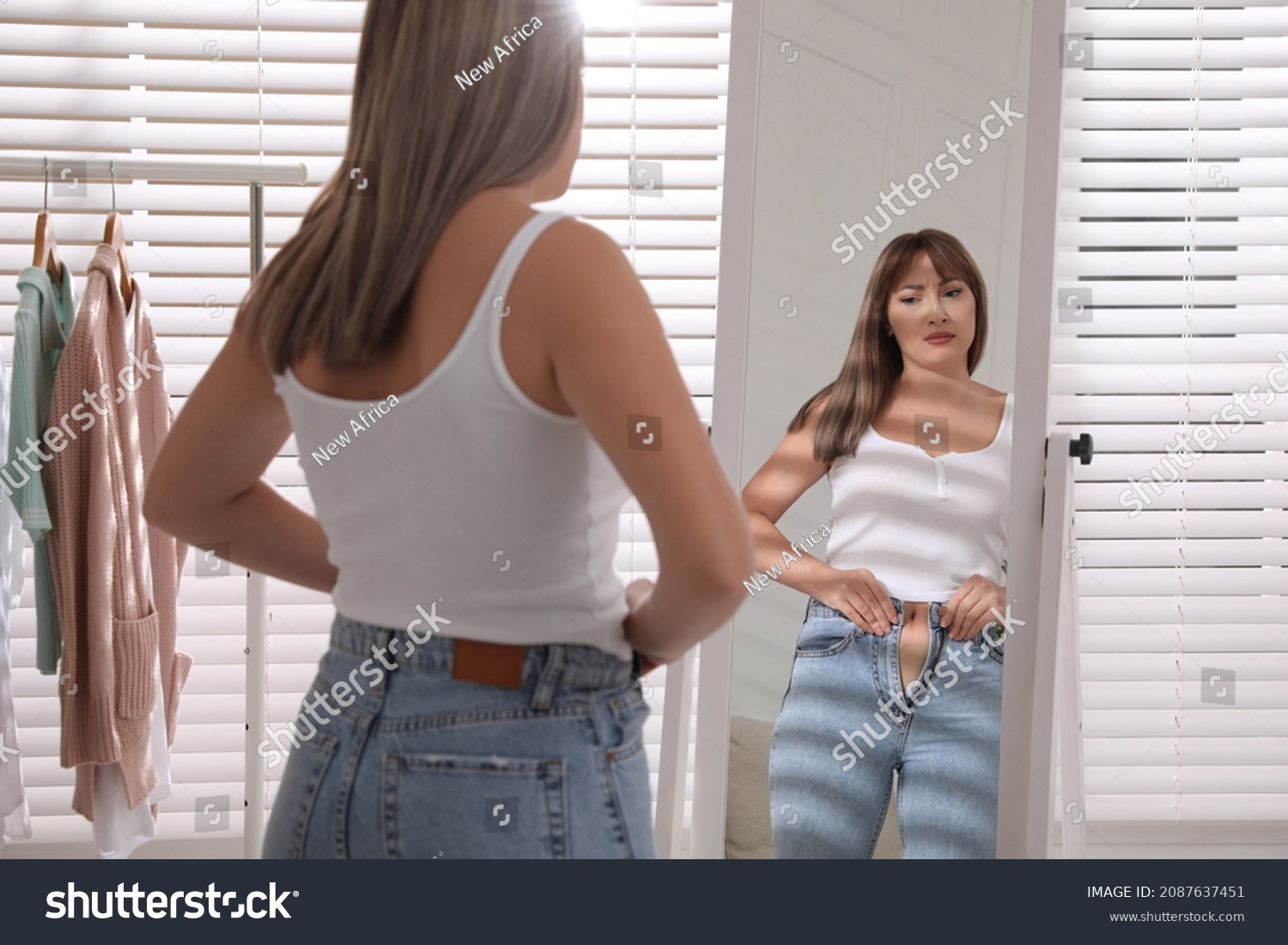 Young woman trying to put on tight jeans near mirror at home #2087637451