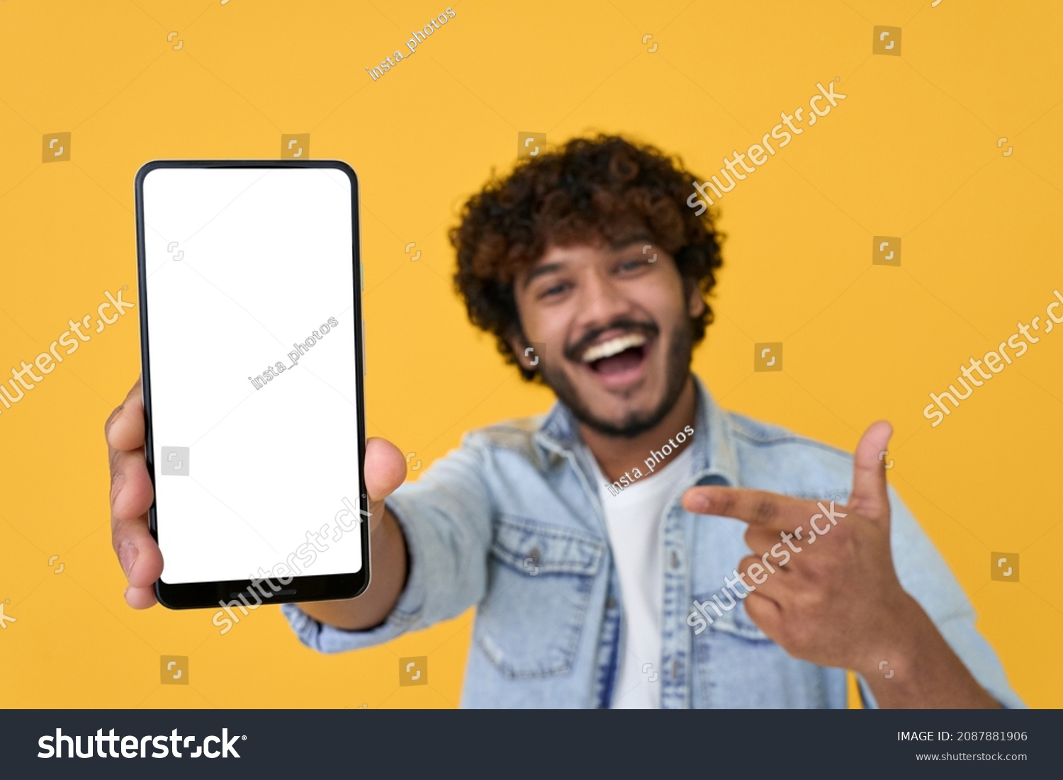 Happy excited young indian man showing smartphone pointing at big mockup white blank phone template screen isolated on yellow background presenting cellphone mobile offer application ads concept. #2087881906