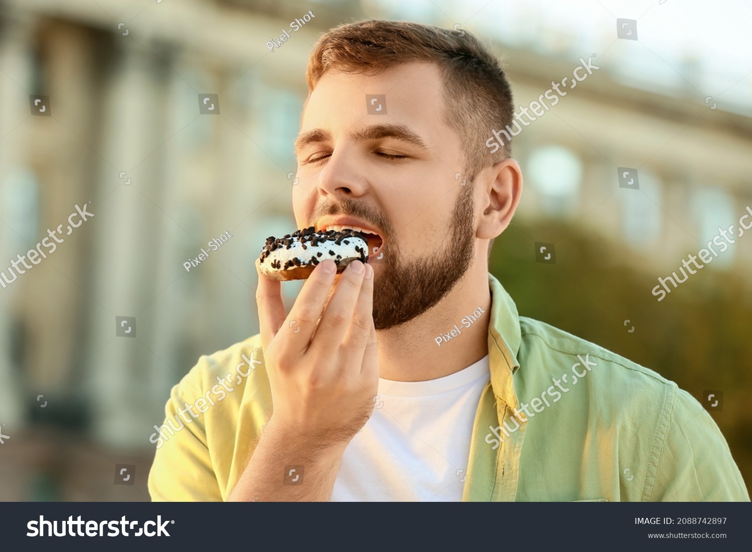 Handsome young man eating sweet donut outdoors #2088742897