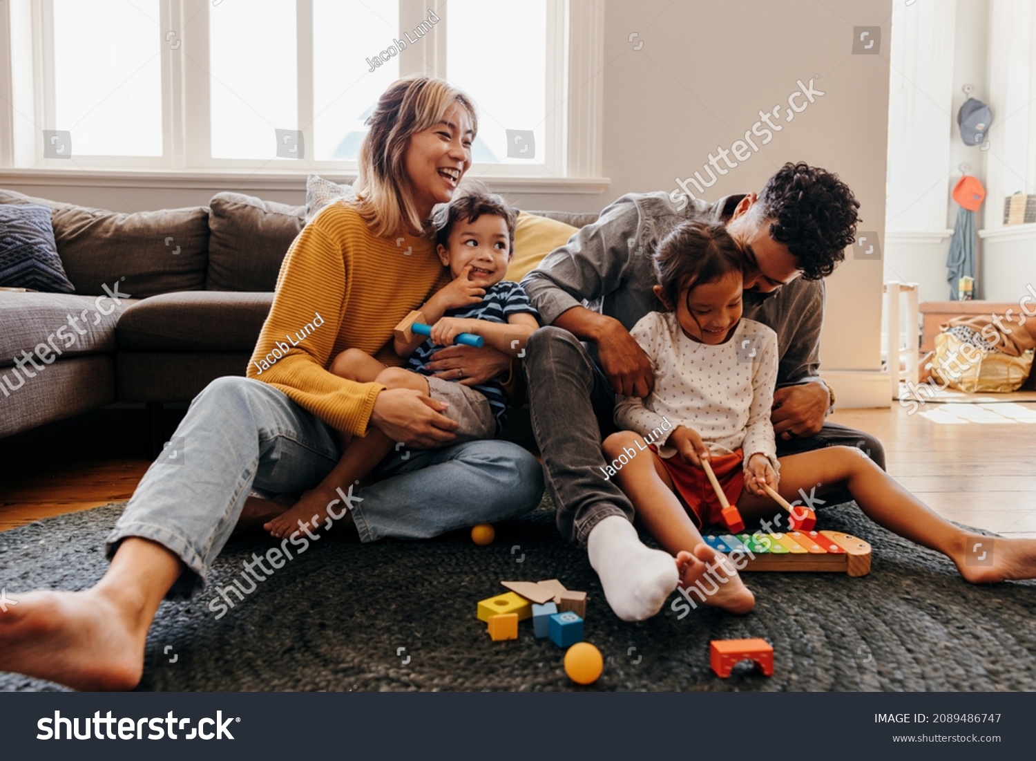 Young parents playing with their son and daughter in the living room. Mom and dad having fun with their children during playtime. Family of four spending some quality time together at home. #2089486747