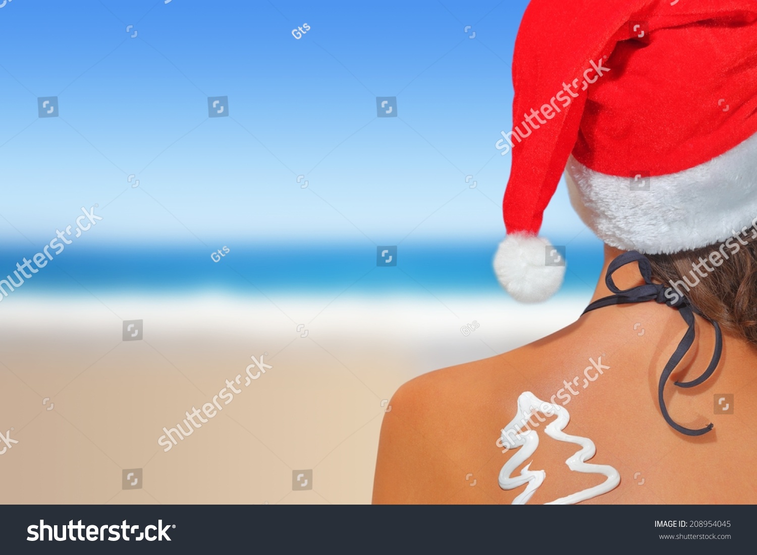 Woman on the beach in santas hat with Christmas tree shaped sunscreen #208954045