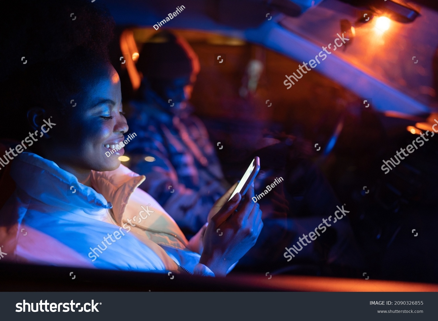 Gadget addicted couple sit in car on parking in silence using smartphones and surfing social media. African american man and woman busy with mobile phones while spending time together. Selective focus #2090326855