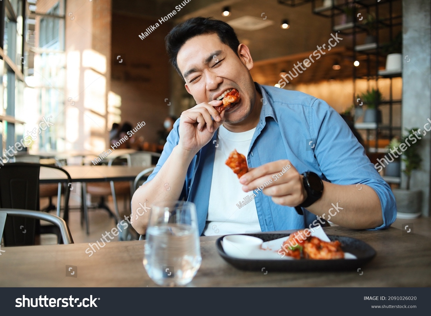 Happy  Asian man eating BBQ chicken wings in restaurant. #2091026020