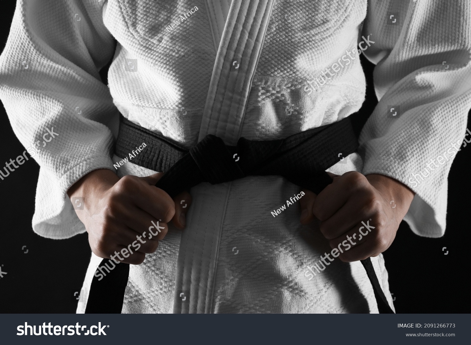 Man in keikogi tying black belt on dark background, closeup. Martial arts uniform #2091266773