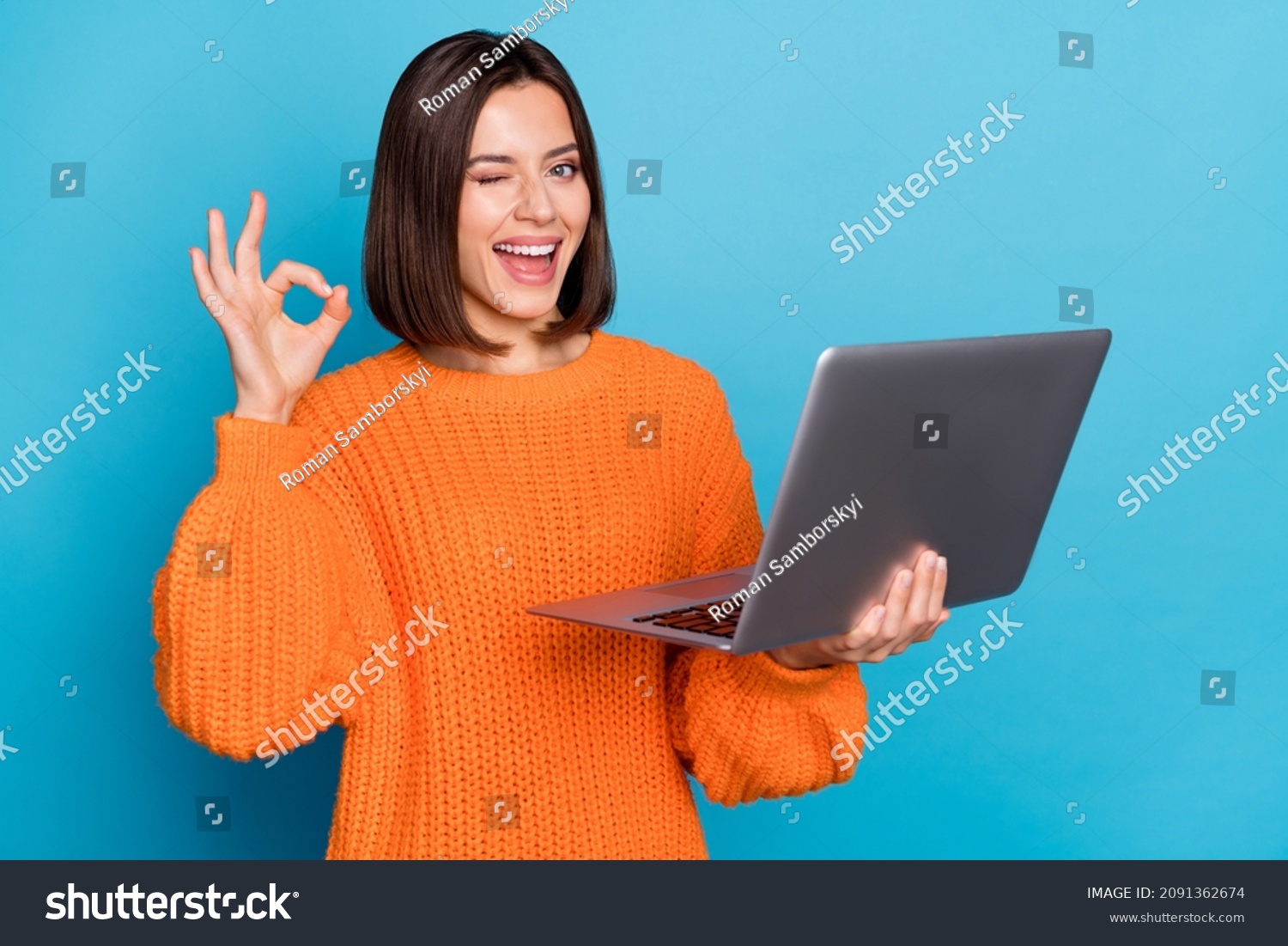 Portrait of attractive cheerful skilled girl using laptop showing ok-sign winking isolated over bright blue color background #2091362674