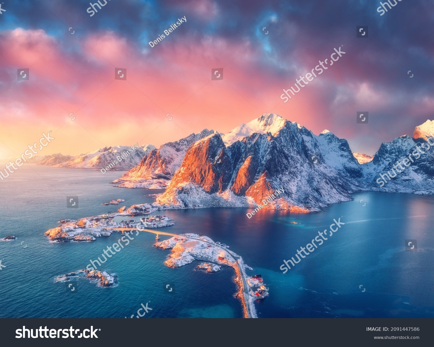 Beautiful landscape with blue sea, snowy mountains, rocks and islands, village, rorbu, road, bridge and pink sky at sunrise. Aerial view. Hamnoy in snow in winter in Lofoten islands, Norway. Top view #2091447586