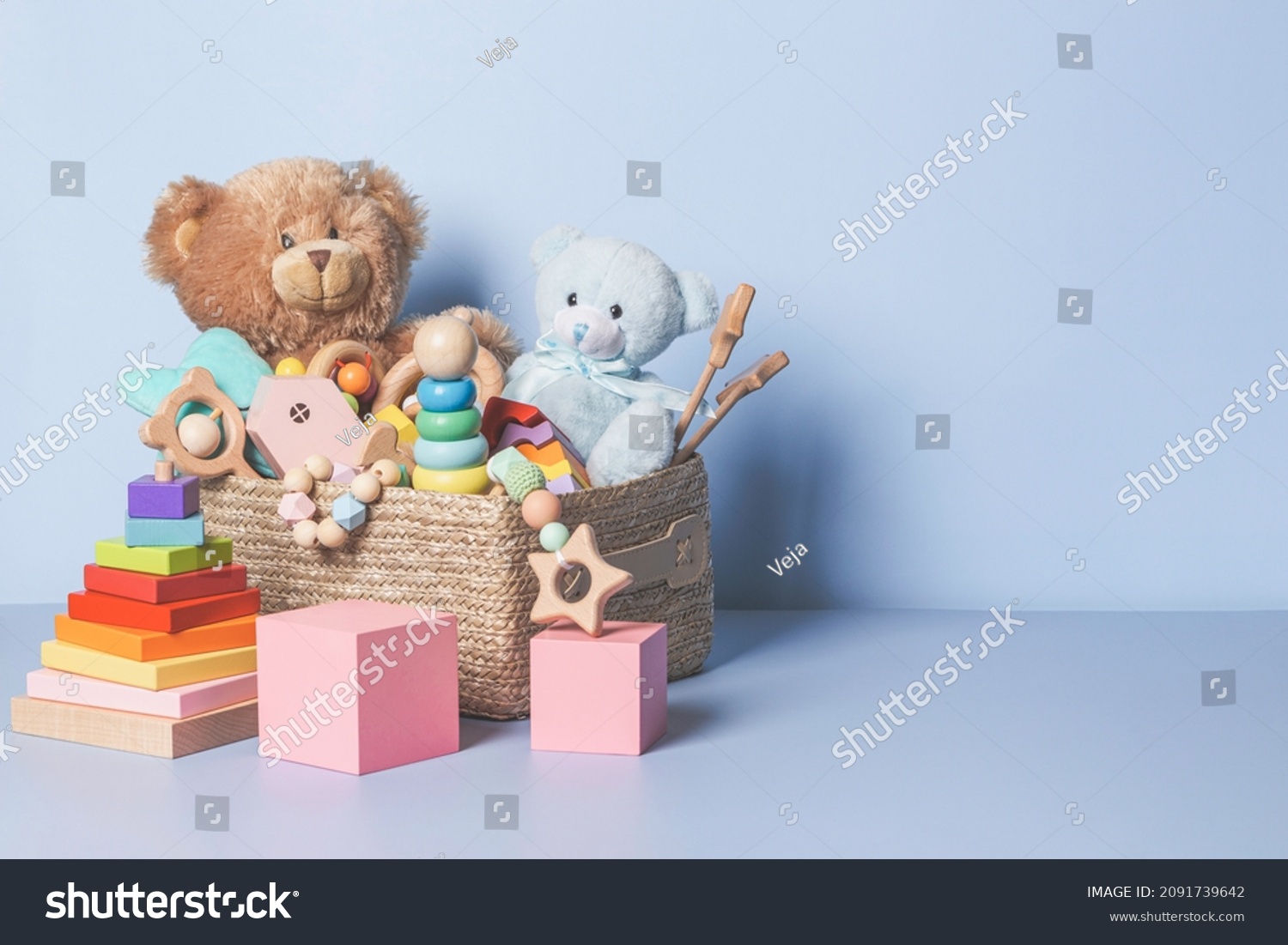 Toy box full of baby kid toys. Container with teddy bear, wooden rattles, stacking pyramid and wood blocks on light blue background. Cute toys collection for small children. Donation. Front view #2091739642