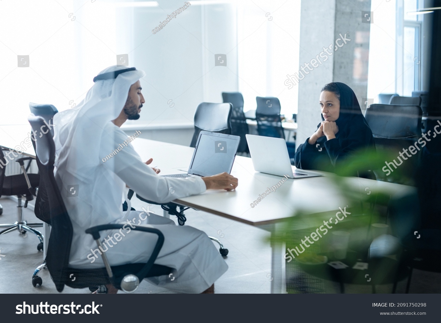 Man and woman with traditional clothes working in a business office of Dubai. Portraits of  successful entrepreneurs businessman and businesswoman in formal emirates outfits. Concept about middle east #2091750298