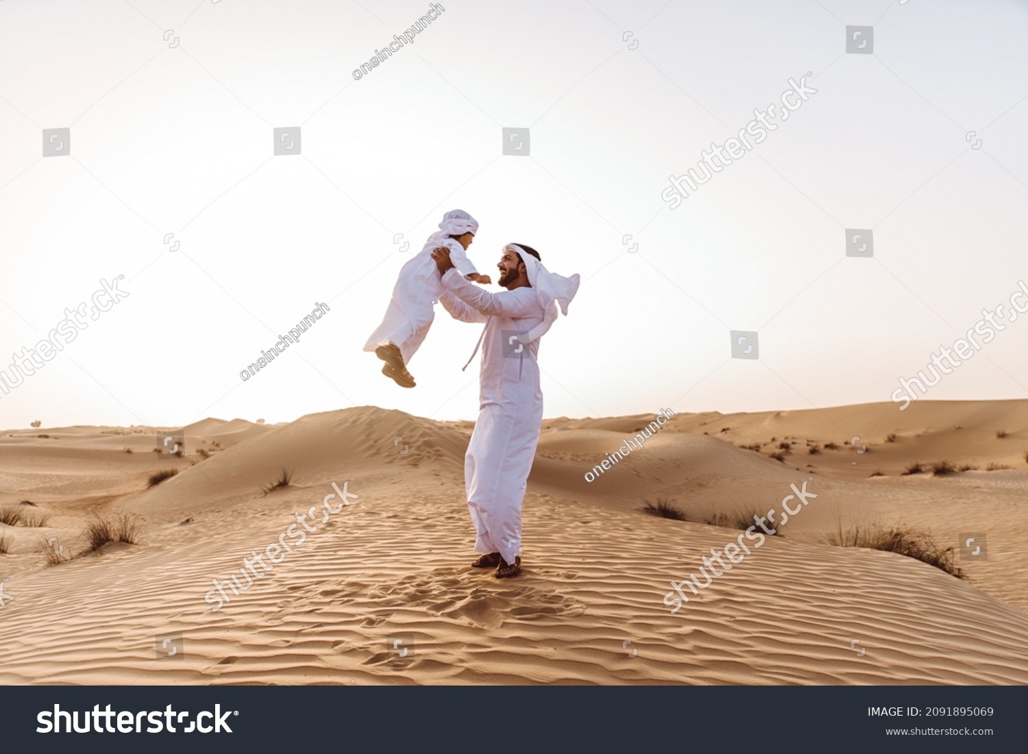 Father and son spending time in the desert on a safari day. Arabian family from the emirates wearing the traditional white dress. Concept about lifestyle and middle eastern cultures #2091895069