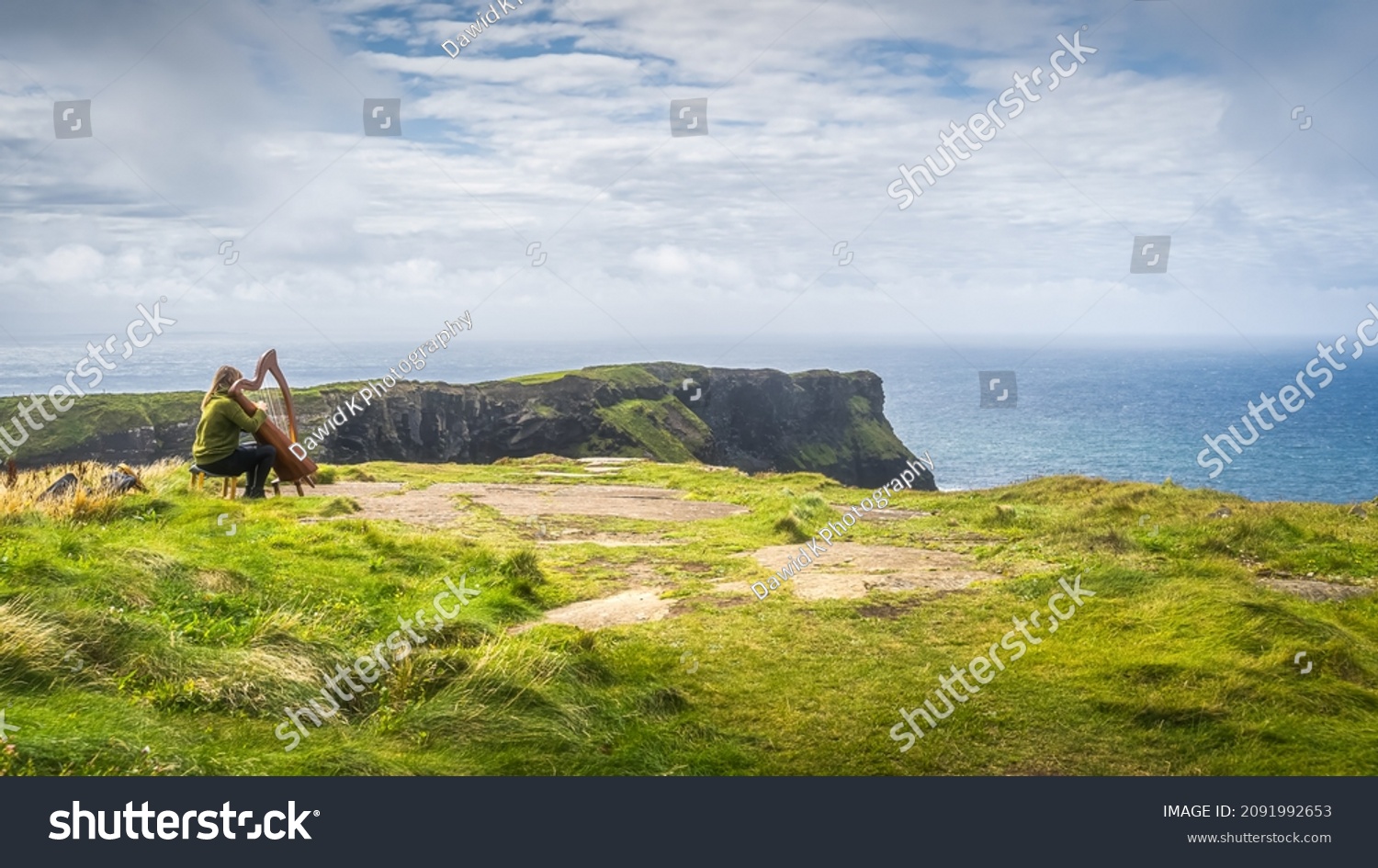 Woman playing harp on the top of the cliff with stunning view on iconic Cliffs of Moher, popular tourist attraction, Wild Atlantic Way, Clare, Ireland #2091992653