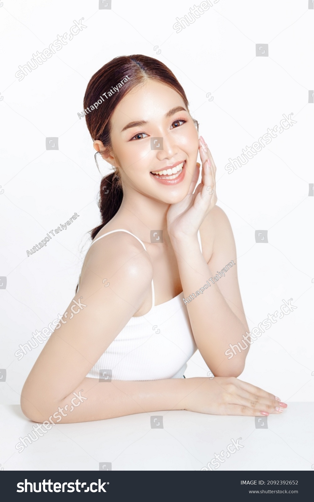 Asian woman with a beautiful face gathered in a brown ponytail and clean fresh smooth skin. Cute female model with natural makeup and sparkling eyes on white isolated background. #2092392652