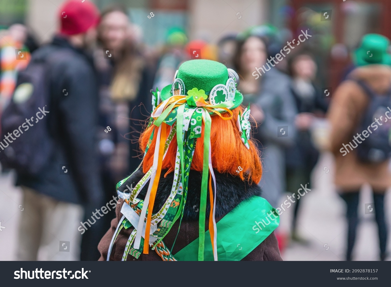 Back view of girl with red hair in hat with decorations, symbols of St. Patrick's Day, parade in city #2092878157