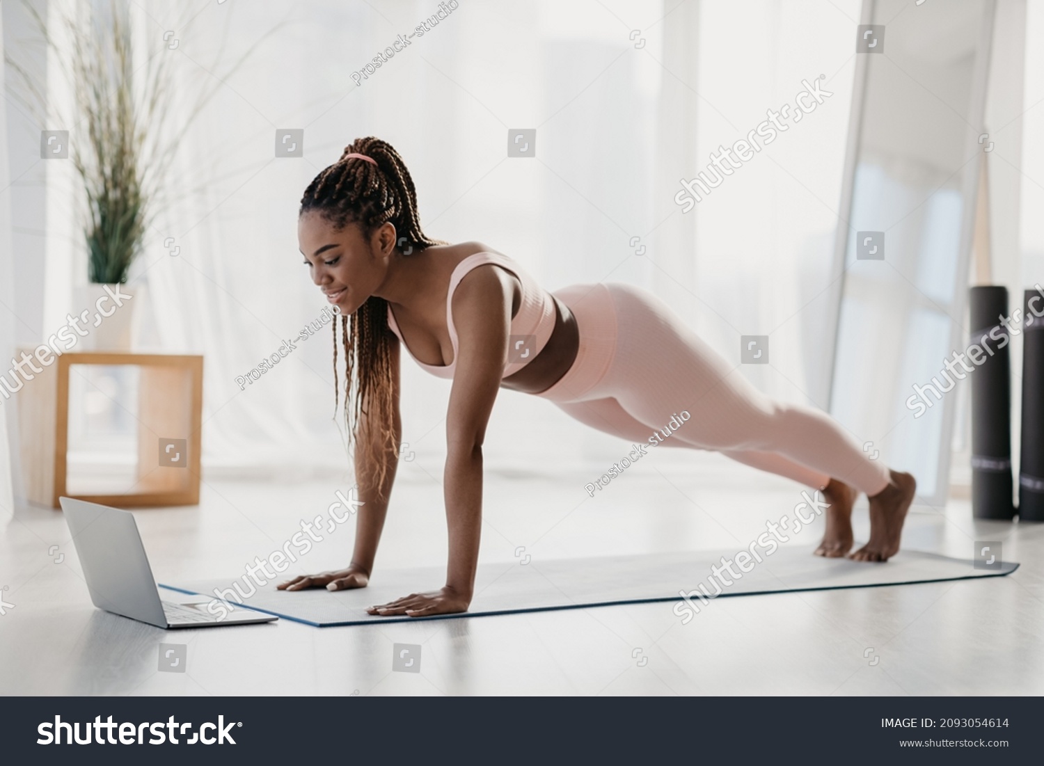 Full length of sporty young black woman standing in plank, training to online sports video on laptop at home. Athletic African American lady exercising abs muscles, doing domestic workout #2093054614