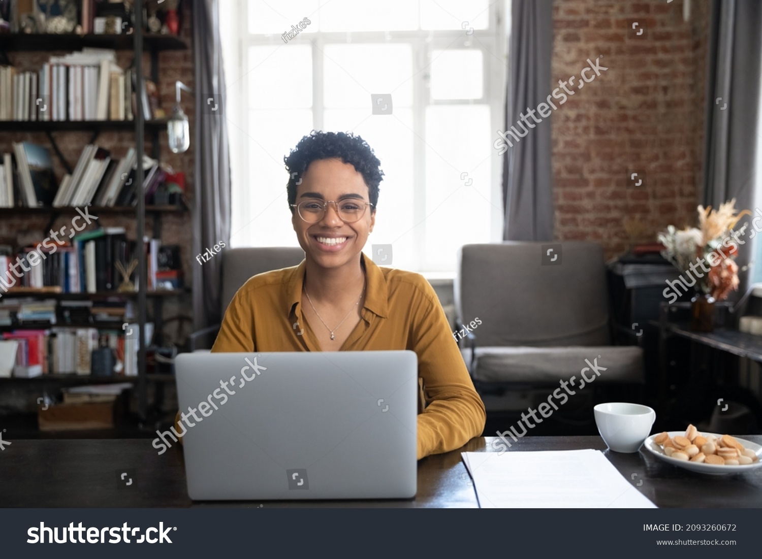 Portrait of happy young African American woman in eyewear sitting at table with computer. Smiling successful millennial female entrepreneur posing in modern loft style office room, feeling motivated. #2093260672