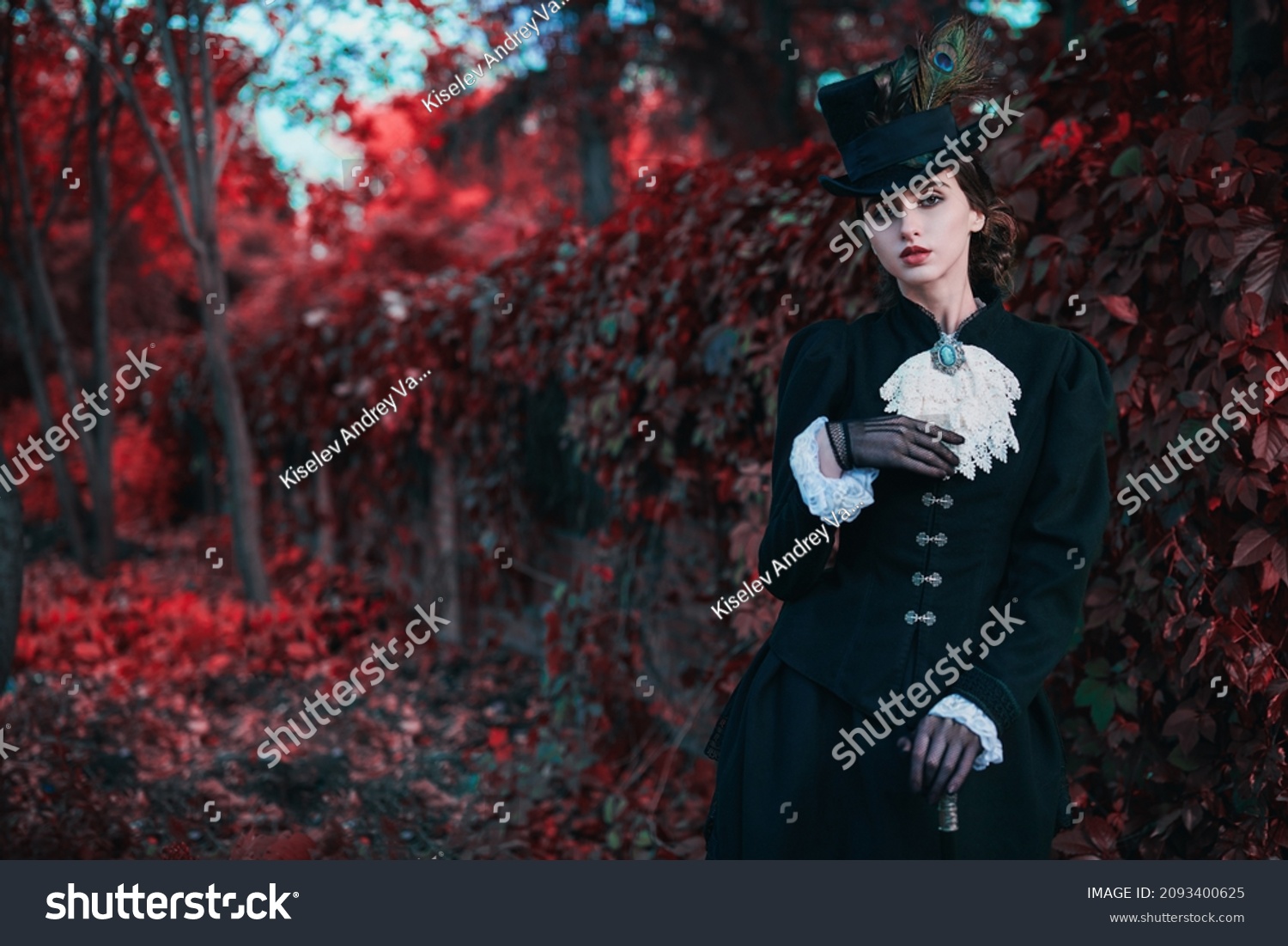Historical reconstruction of the late 19th and early 20th centuries. Elegant brunette lady in a strict black dress posing in the background of red foliage. Historical makeup and hairstyle. #2093400625