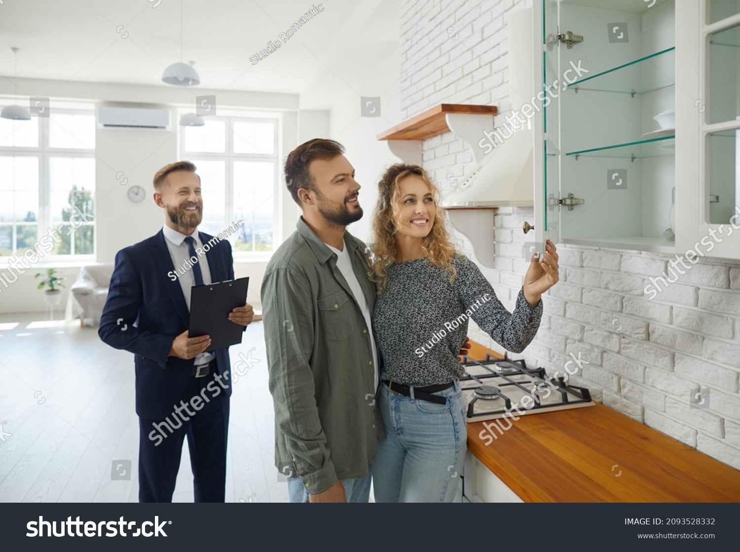 Realtor with customers checking apartmnet. Couple examines furniture in kitchen while inspecting house with real estate agent. Friendly male realtor advises young family before buying new home. #2093528332