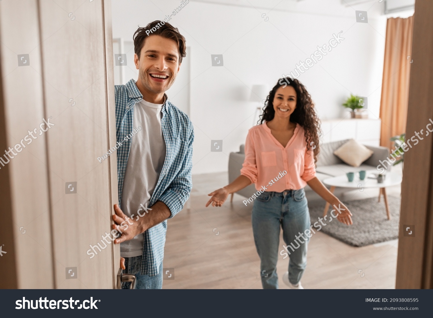 Portrait of cheerful couple welcoming inviting guests to enter home, happy young guy and lady standing in doorway of modern flat, looking out together, waiting for visitor friends to come in #2093808595