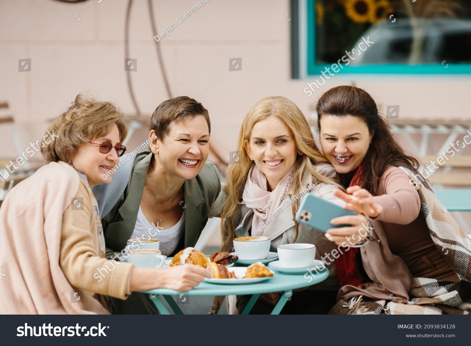 Three Caucasian pretty senior women friends sitting with coffee at table in cafe terrace and smiling to smartphone camera while taking selfie photos. Old ladies posing to phone. Pensioners resting. #2093834128