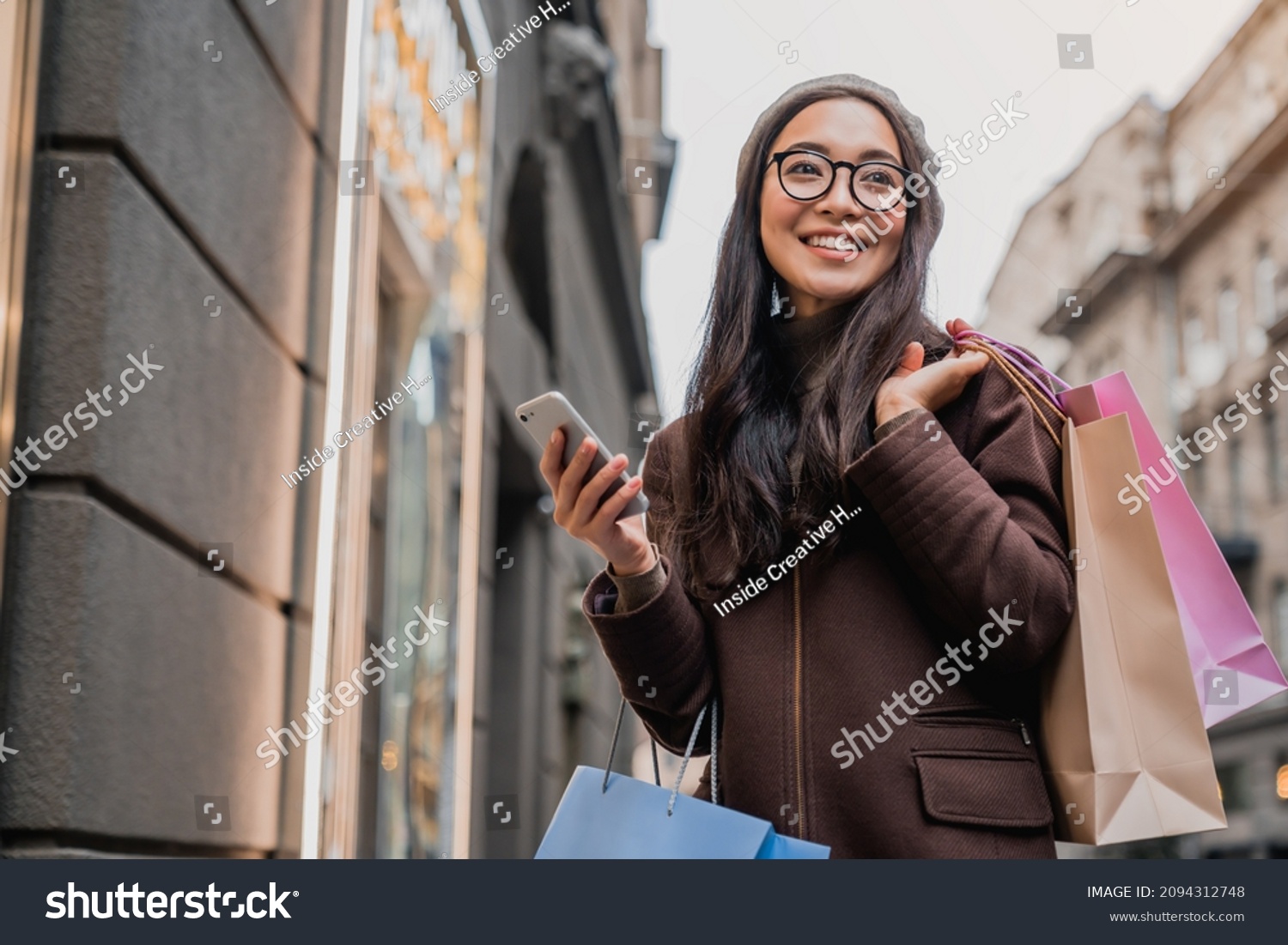 Asian woman using smartphone and looking away while enjoying a day shopping. Black friday, sale and discount. Buying clothes presents for holidays #2094312748