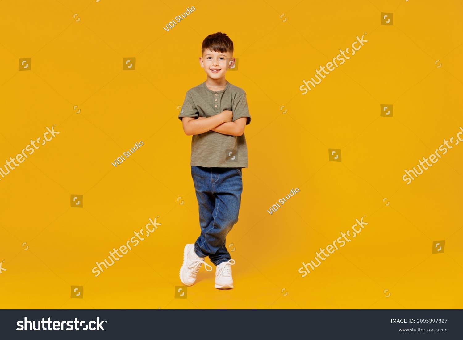 Full body little small smiling happy boy 6-7 years old wearing green t-shirt hod hands crossed folded look camera isolated on plain yellow background studio Mother's Day love family lifestyle concept #2095397827