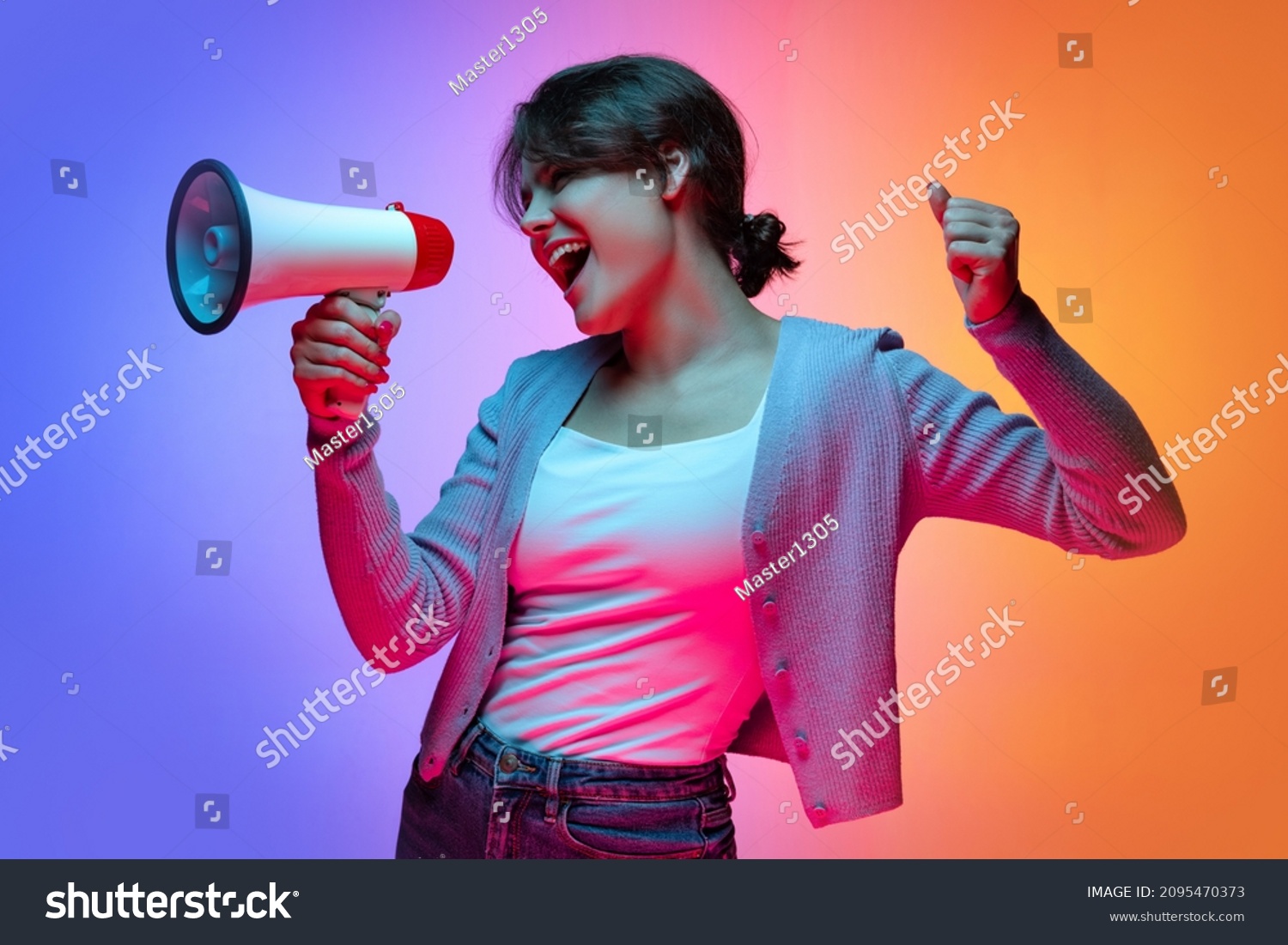 Attention, news. Excited young beautiful girl in warm cardigan shouting at megaphone isolated on gradient blue orange neon background. Concept of emotions, facial expression, youth, aspiration, sales #2095470373