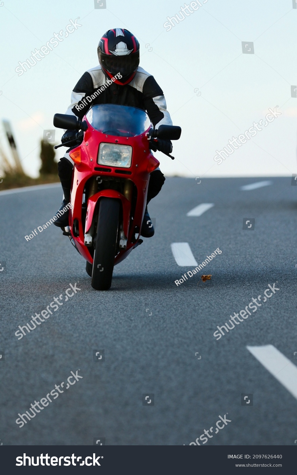 Red motorcycle with driver in leather suit while driving on a road with a slight side position, photographed from the front.
 #2097626440