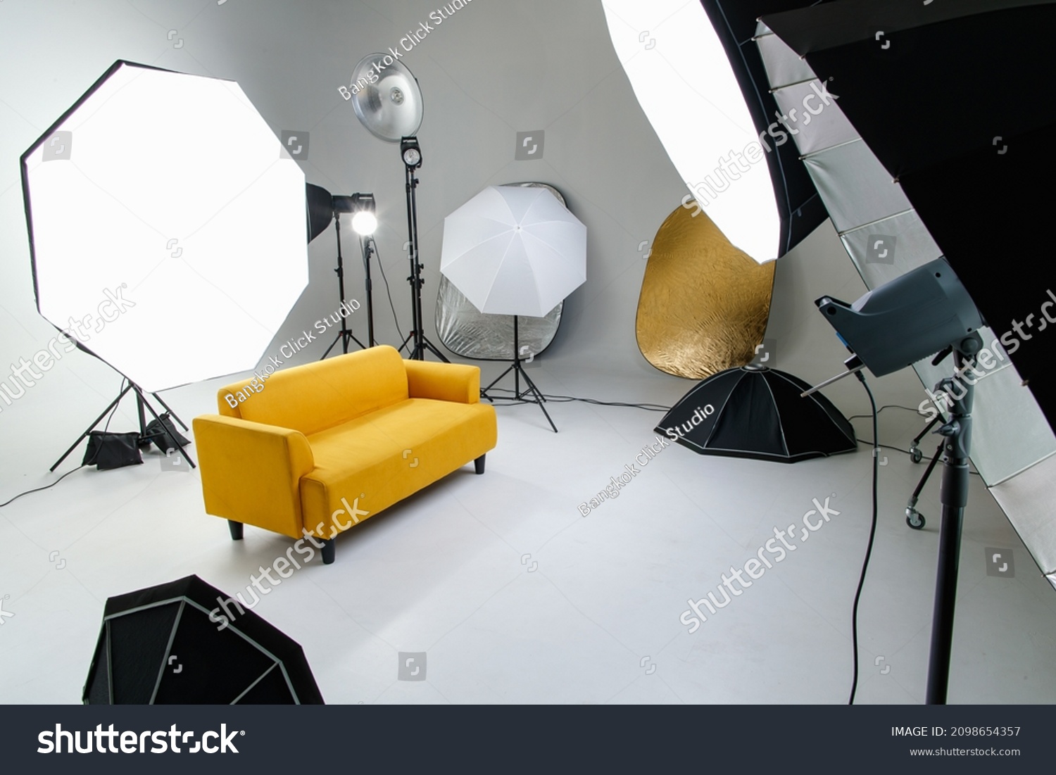 Studio shot fashion backstage photographing shooting set with yellow cozy sofa couch and photography equipment softbox flash strobe spotlight tripods reflector umbrella on white backdrop background. #2098654357